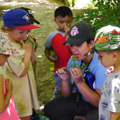 A camp leader crouches on the trail to show young children a plant.