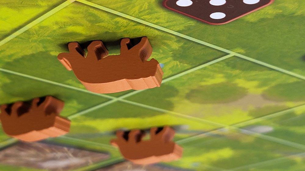 Wooden tigers stand on a forest game board, with deforestation tiles encroaching behind them.