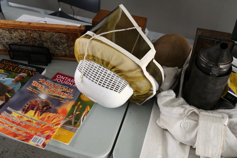 A table display includes a smoker, a beekeepers helmet, and numerous books.