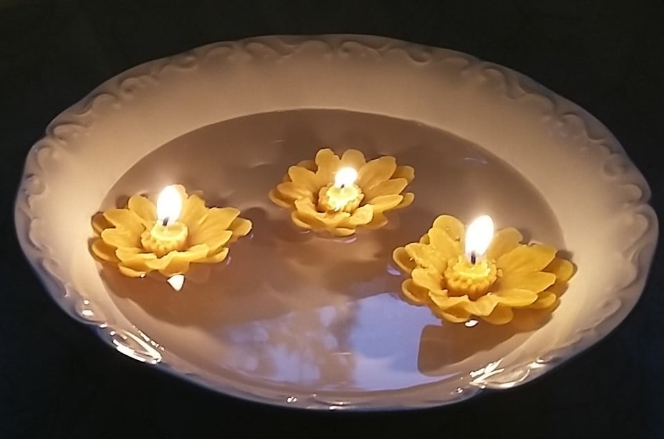 Three lit flower-shaped candles float in a bowl of water