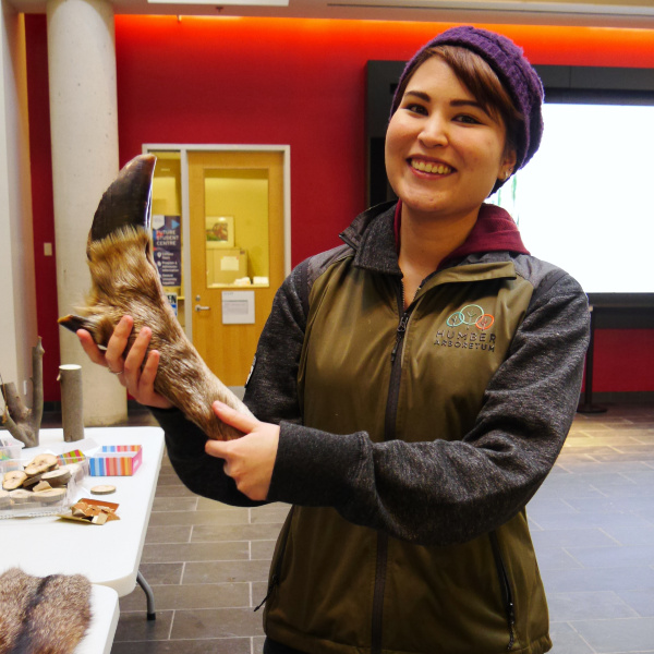 A person at a display booth smiles at they hold up the taxidermied leg of an elk