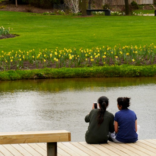 Two young women take a photo by a pond