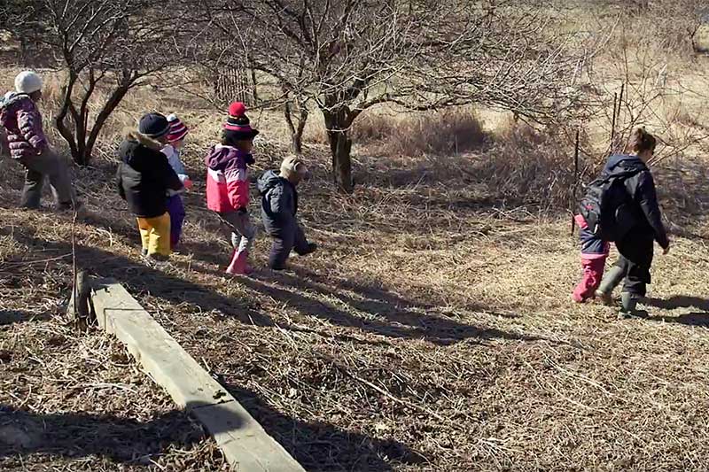 Small children in snow suits walk down a hill covered in dry grasses