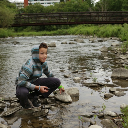 A young man crouches on rocks in the Humber River