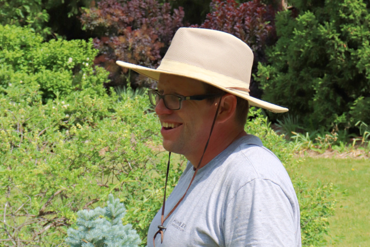 A man in a wide-brimmed hat smiles in a garden.