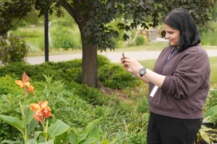 A young woman uses her cellphone to take a photo of a flower in bloom