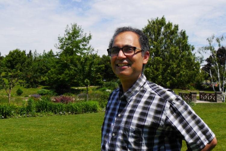 A man in a plaid dress shirt smiles as he looks off across a garden on a sunny day