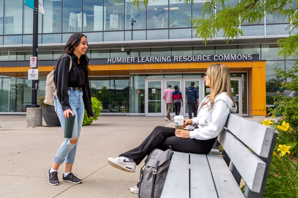 Two students talking on bench outside Humber Learning Resource Commons