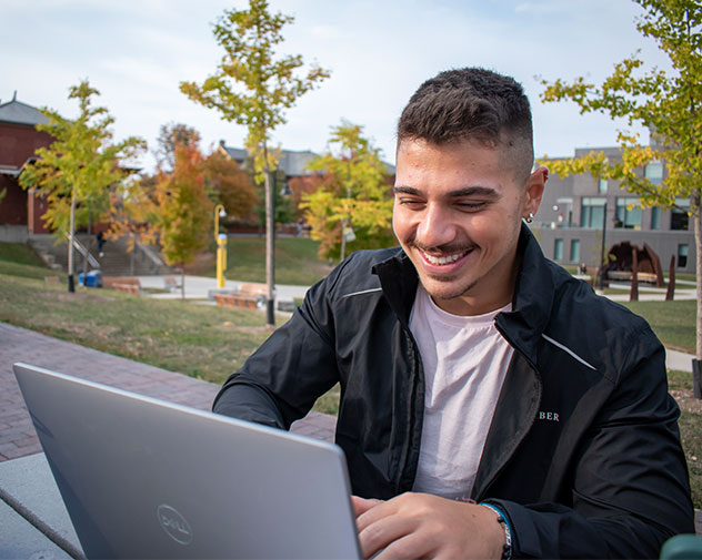 student sitting outside smiling and using a laptop