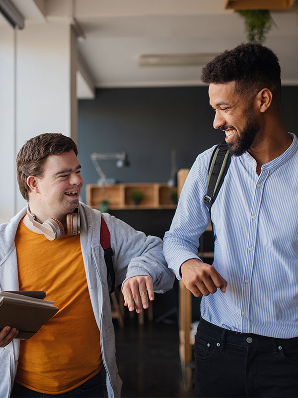 Young happy man with Down syndrome with his mentoring friend celebrating success indoors at school