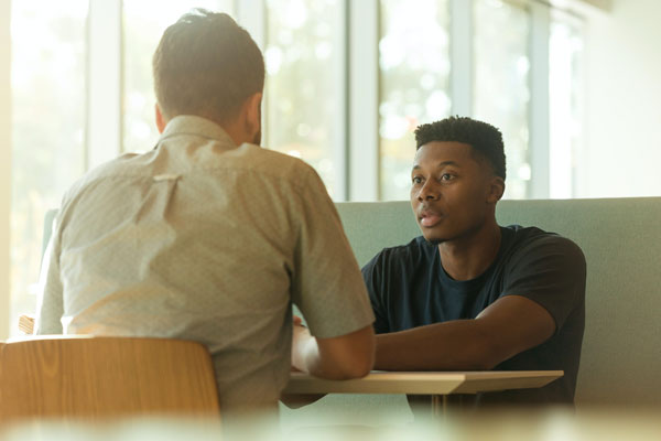 Young man sitting across the table from another person, they are in conversation