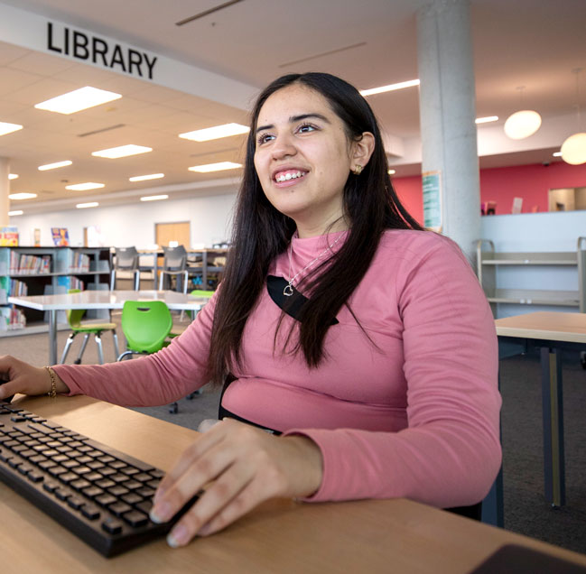 Student working on computer in library smiling