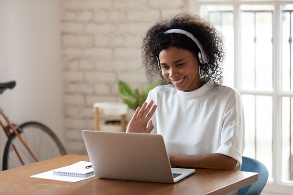 woman wearing headphones waving to her laptop screen