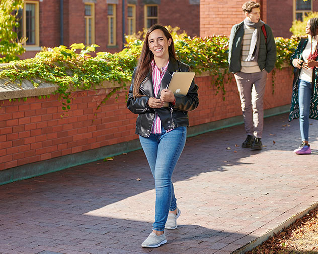 person walking outside smiling and holding a laptop