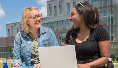 Two females sitting outside on a bench talking