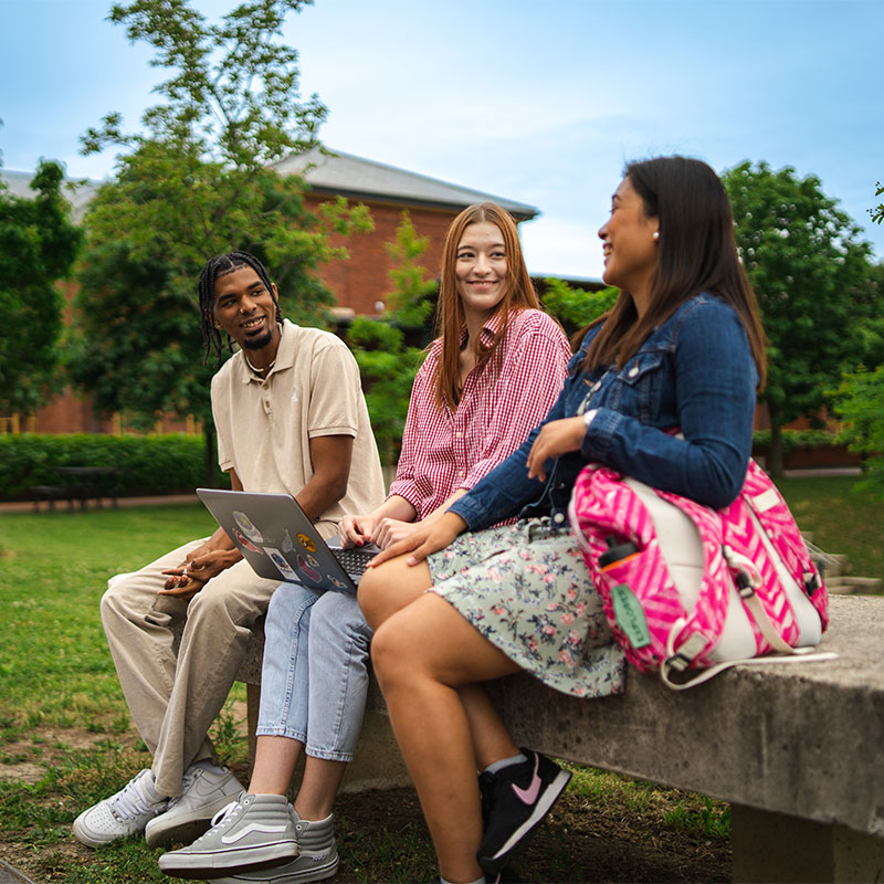 three people sitting outside on a bench talking and laughing