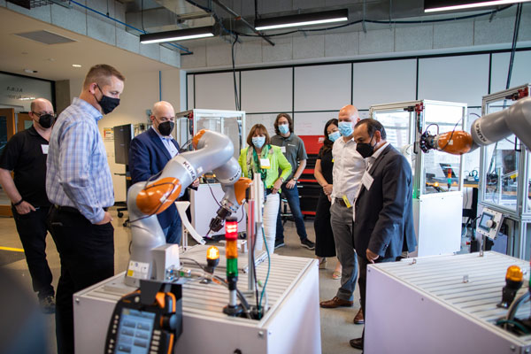 a group people looking at a partner robot arm