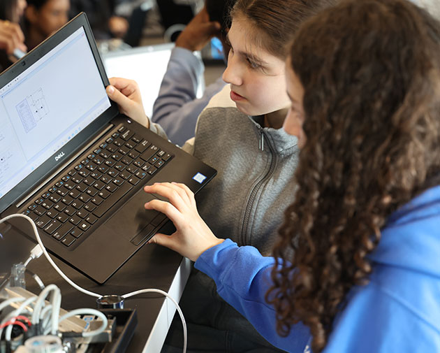 two students collaborating intently on a circuit or robotics interface on a laptop