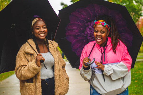 students outside holding umbrellas laughing and smiling