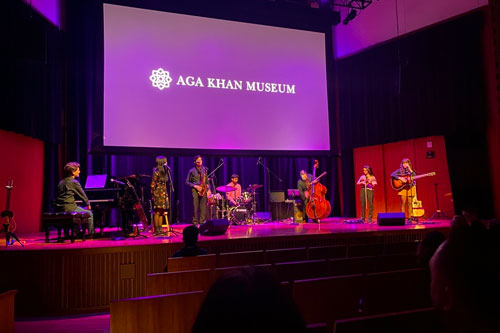 classical musicians playing on stage in a dimly lit room with a projection of the words Aga Kham Museum behind them