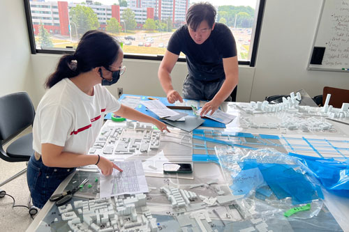 two Tiny T.O. Interns working over scale replica pieces of the city