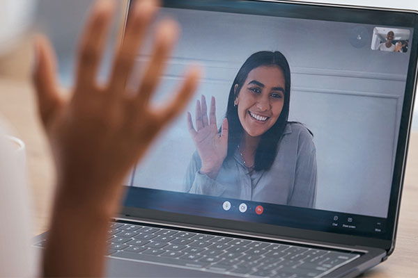 person sitting at a laptop waving to a person on the webcam