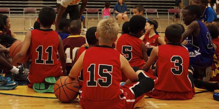 children in basketball uniforms sitting in a gymnasium