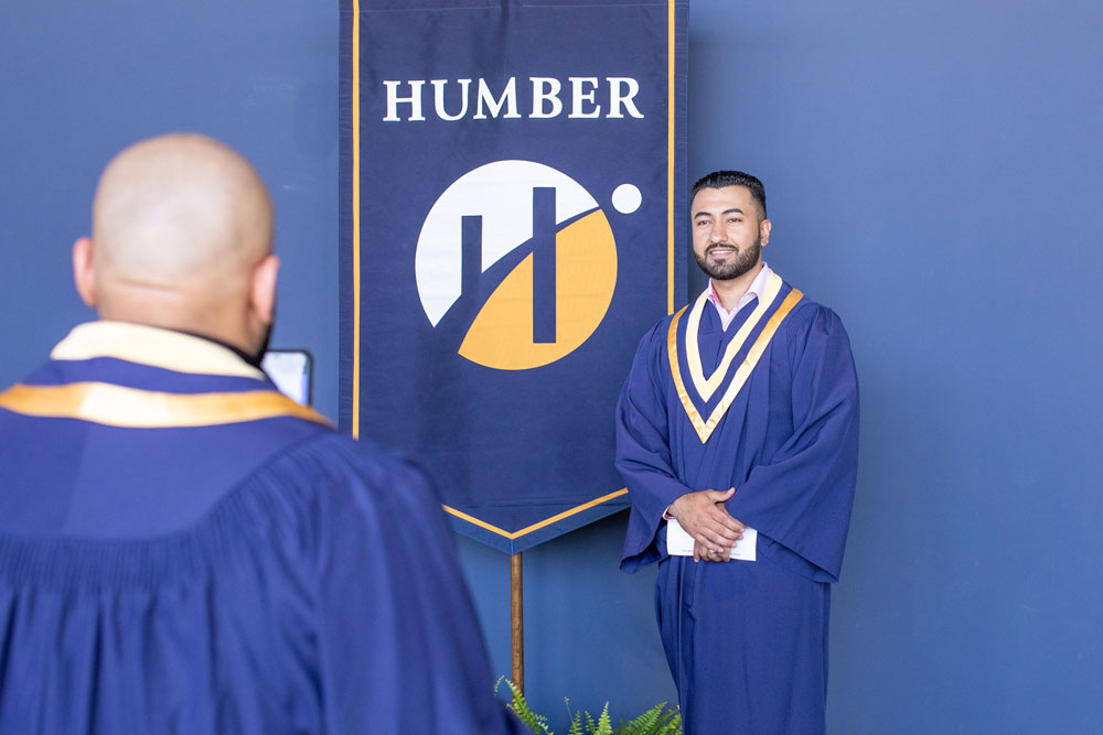 Humber graduate standing next to a Humber banner with their hands clasped