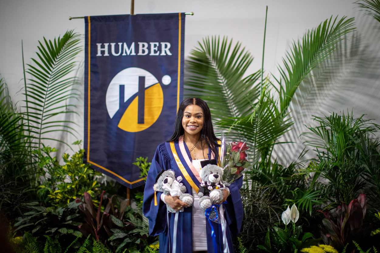 graduate with teddy bears in front of Humber banner