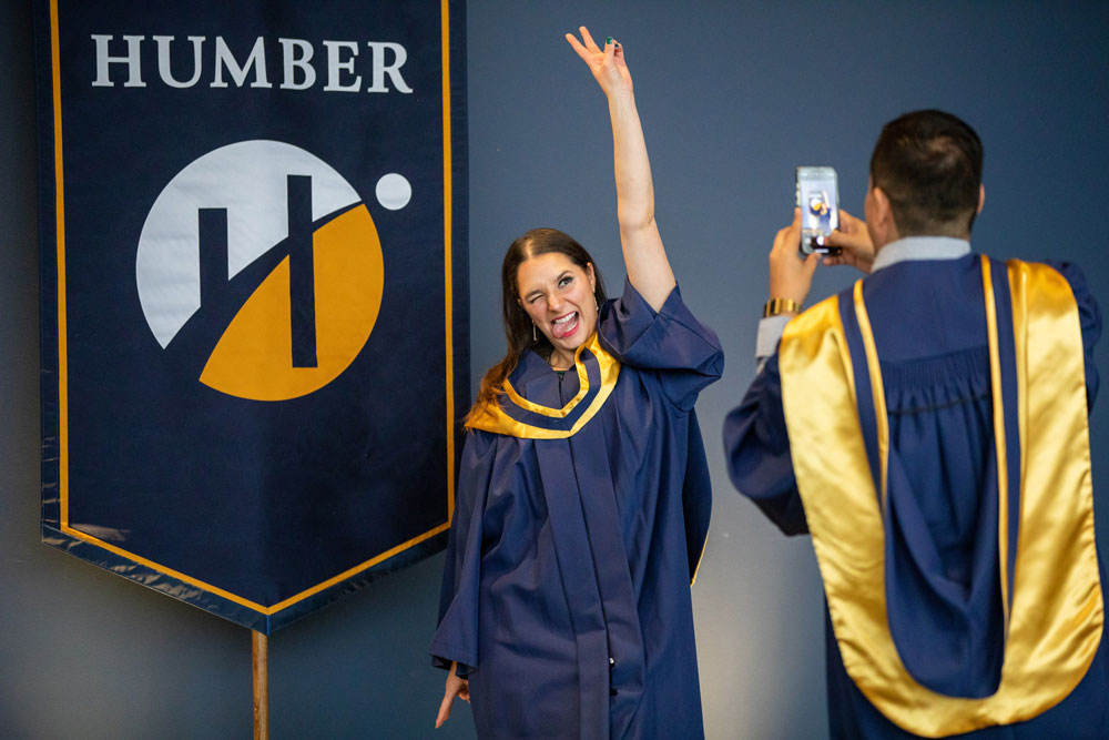 Grad taking picture of another grad in front of Humber banner