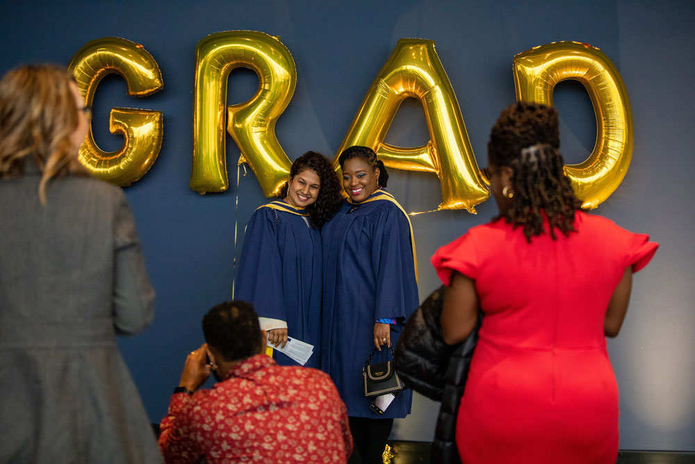 Two grads getting pictures taken in front of gold GRAD balloons