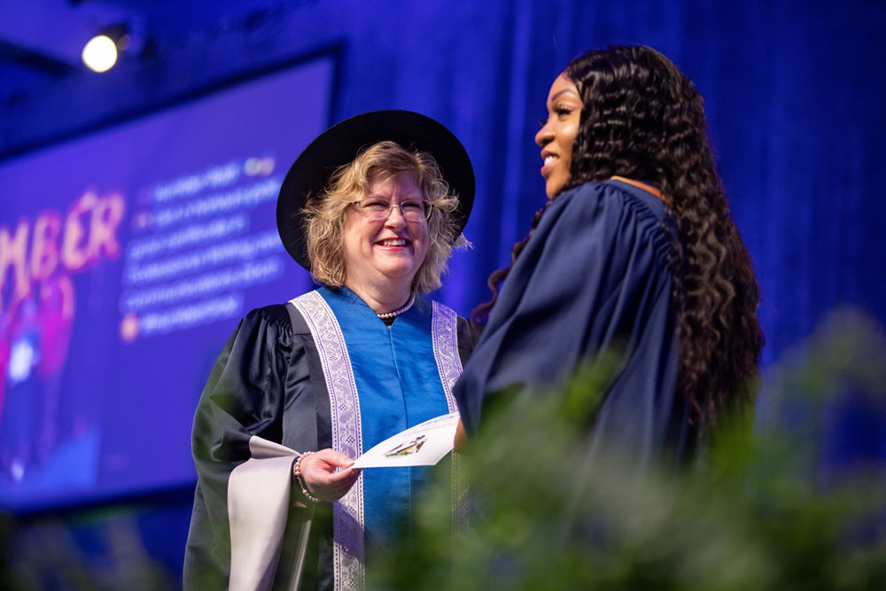 Humber president smiling and presenting certificate to graduate