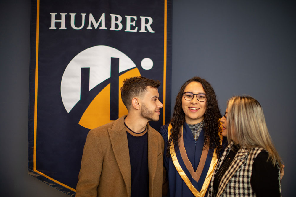Grad posing with two people in front of Humber banner