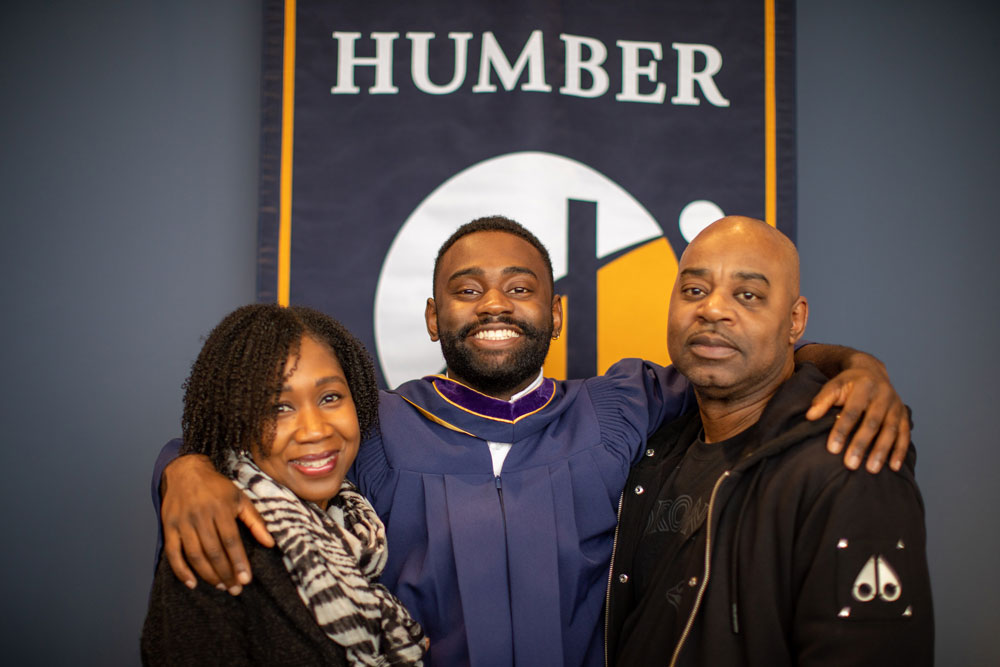 Grad with parents in front of Humber banner