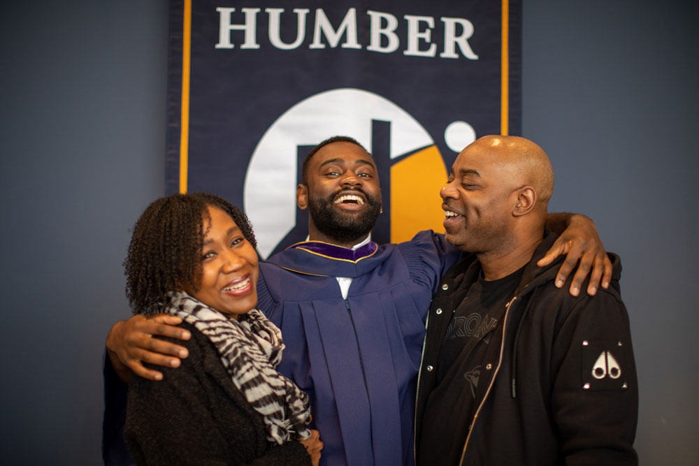 Grad smiling with parents in front of Humber banner