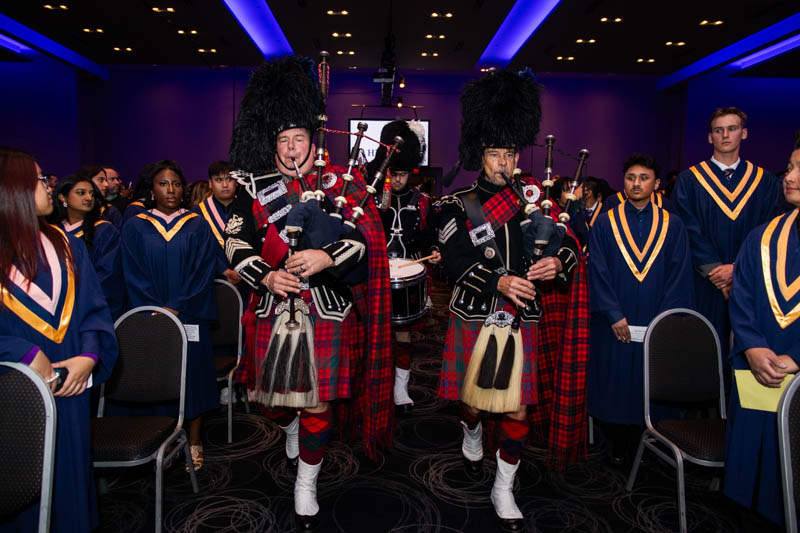 People in Scottish regalia play bagpipes as they walk down aisle