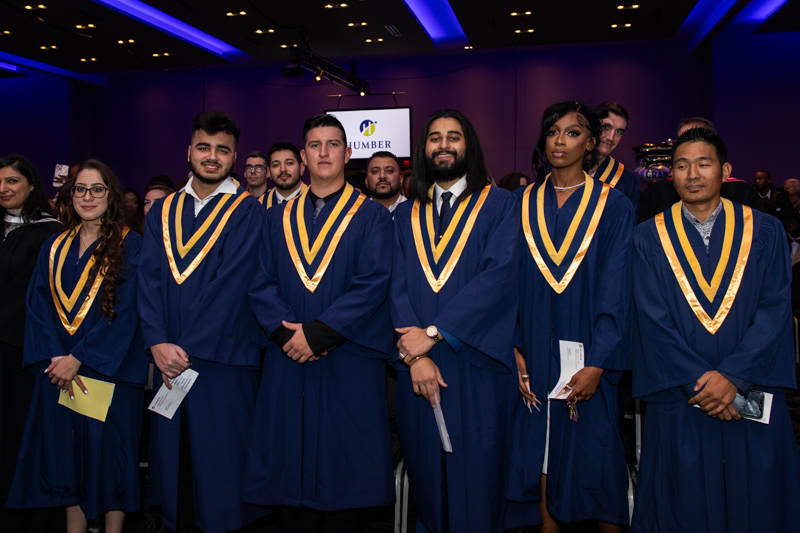 Graduates standing in ceremony hall look at camera