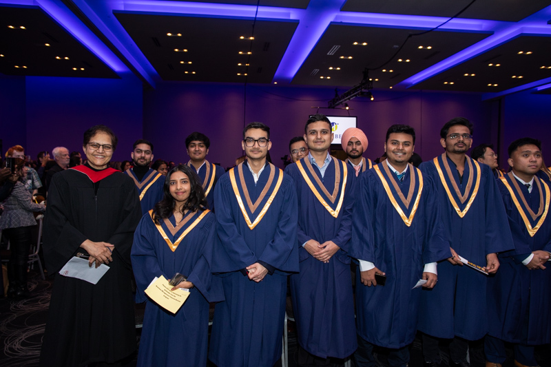 Graduates standing in ceremony hall look at camera