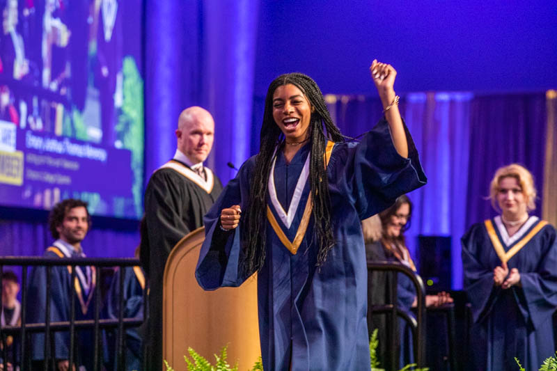 Graduate leaving stage with one arm raised in celebration