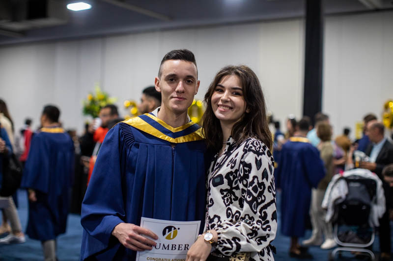 Graduate and ceremony guest pose for photo
