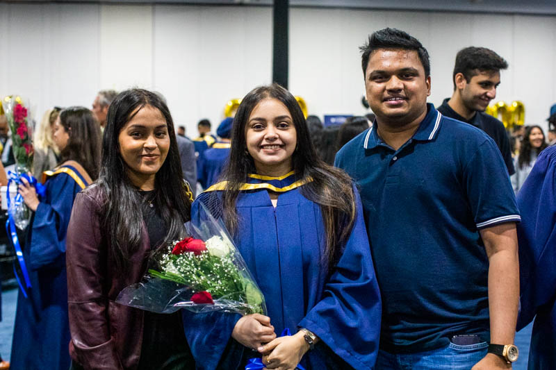 Graduate holding flowers poses for photo with two guests
