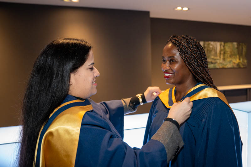 Student helping other with gown