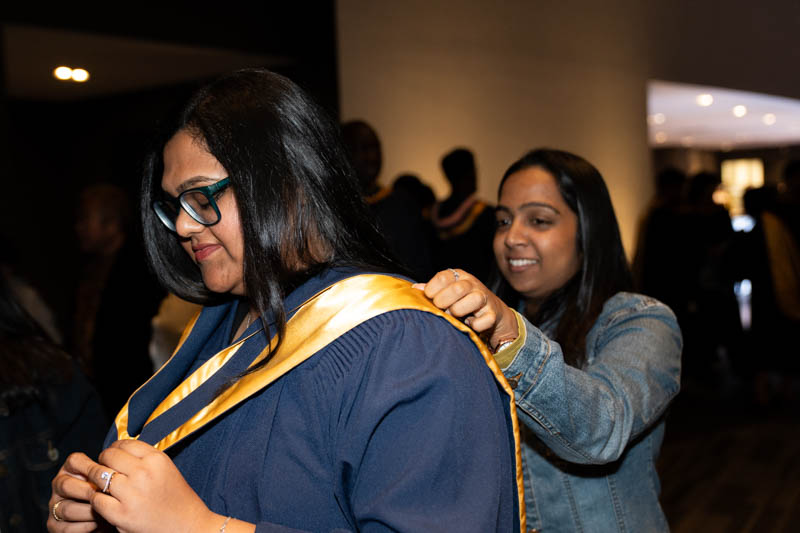 Student helping other with gown