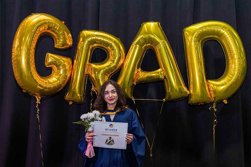 Student holding diploma in front of Grad Balloons