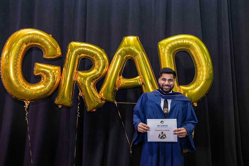 Student holding diploma in front of Grad Balloons