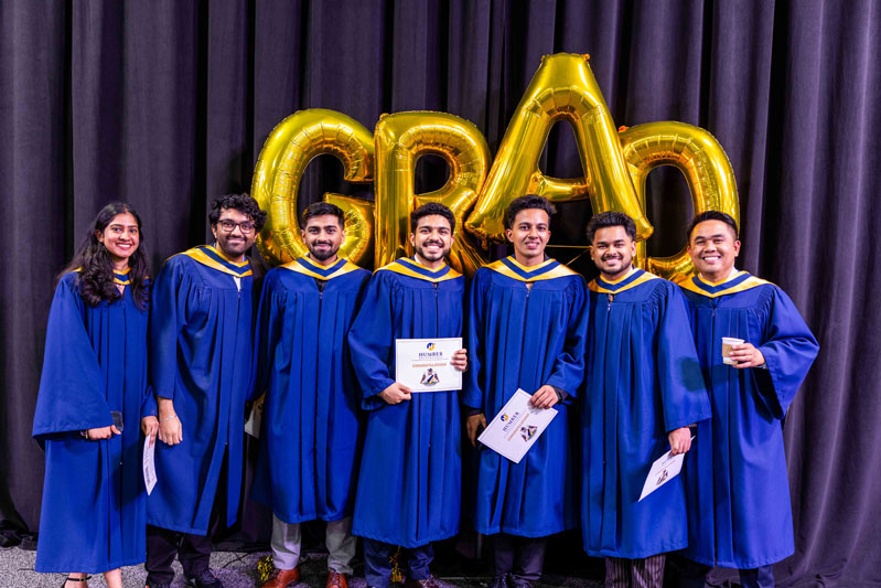Student posing for picture with diplomas in front of Grad Balloons
