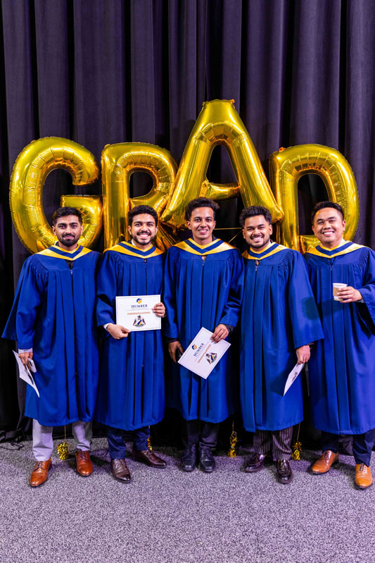 Student posing for picture with diplomas in front of Grad Balloons