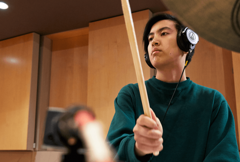 Young man playing drums while wearing headphones.