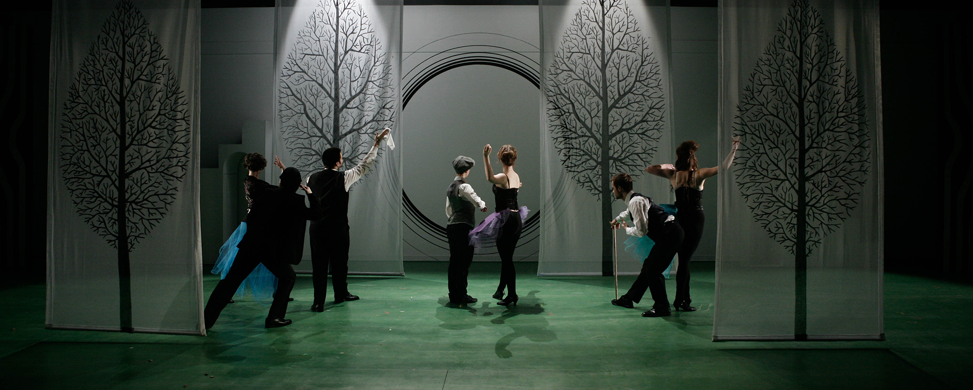 Seven performers on a stage with moody lighting and tree backdrops