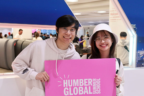 2 students at airport holding Humber sign